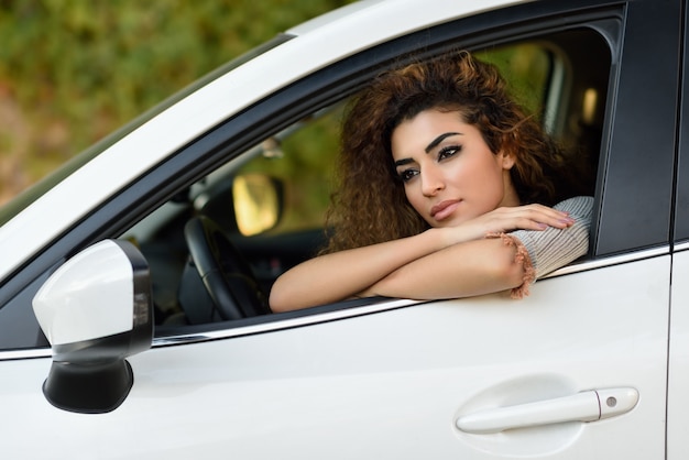 Young arabic woman inside a white car looking through the window