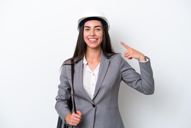 Young architect caucasian woman with helmet and holding blueprints isolated on white background giving a thumbs up gesture