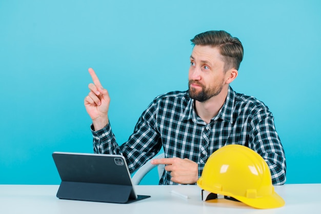 Young architect is pointing up with forefinger on blue background