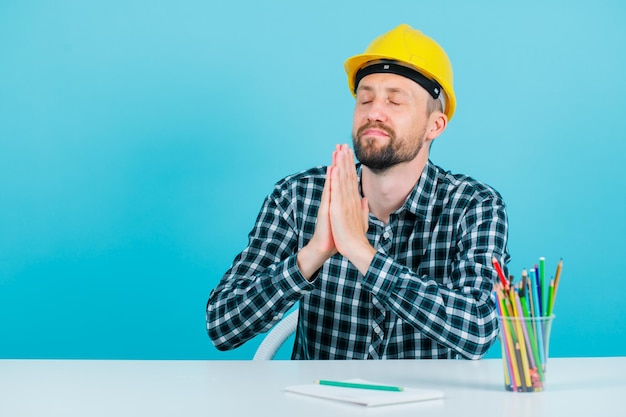 Young architect is praying by holding hands together on blue background