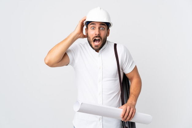 Young architect man with helmet and holding blueprints isolated on white background doing nervous gesture