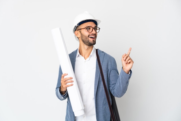 Young architect man with helmet and holding blueprints isolated on white background pointing up a great idea