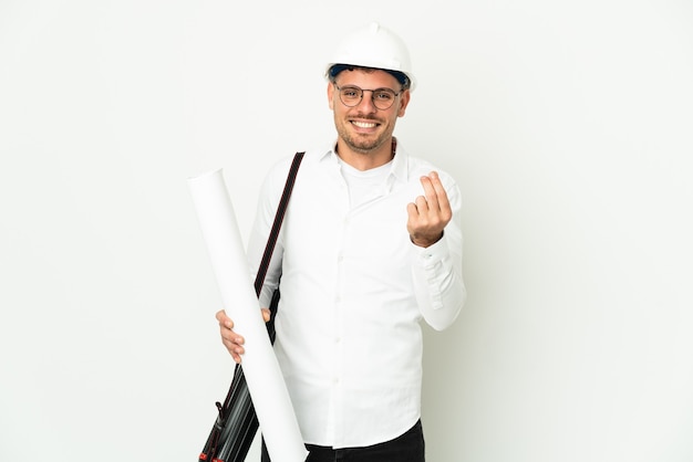 Young architect man with helmet and holding blueprints isolated on white wall making money gesture