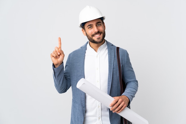 Young architect man with helmet and holding blueprints isolated on white wall showing and lifting a finger in sign of the best