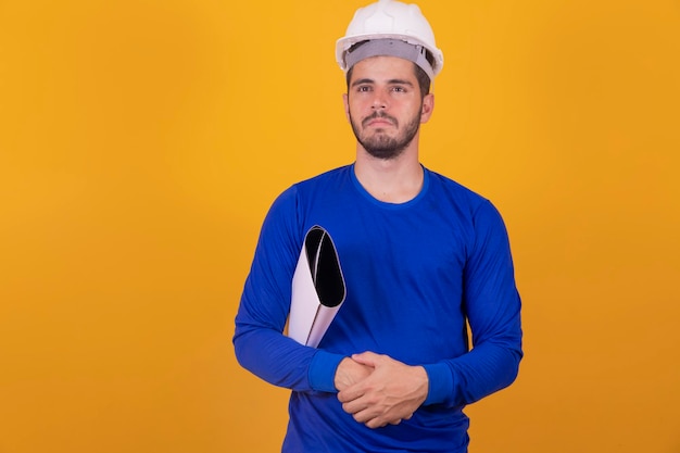 Young architect man with helmet and holding blueprints isolated on yellow background pointing finger to the side