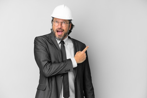 Young architect man with helmet over isolated background surprised and pointing side