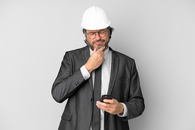 Young architect man with helmet over isolated background thinking and sending a message