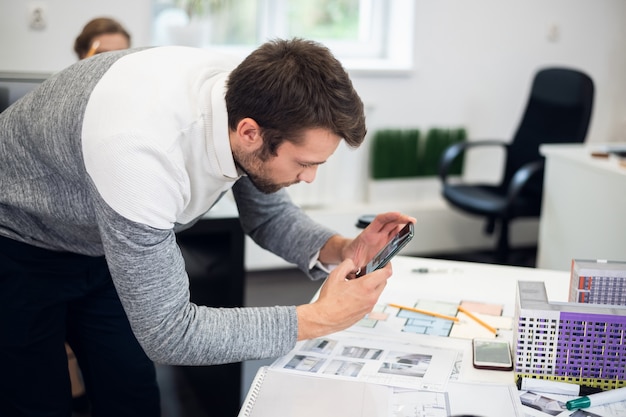 A young architect taking pictures of the construction model while in office