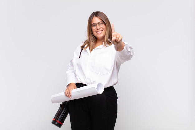 Young architect woman smiling and looking friendly, showing number one or first with hand forward, counting down