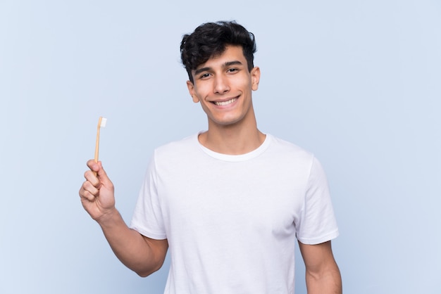 Young Argentinian man brushing his teeth over isolated blue wall smiling a lot