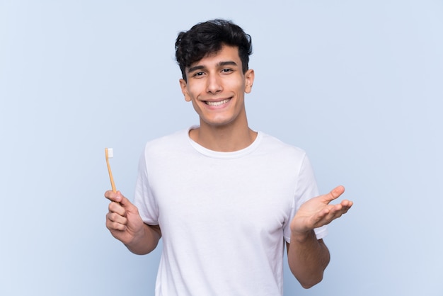 Young Argentinian man brushing his teeth over isolated blue wall with shocked facial expression