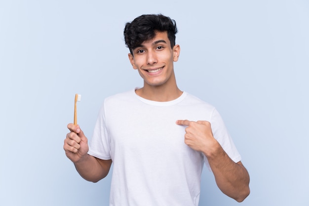 Young Argentinian man brushing his teeth over isolated blue wall with surprise facial expression