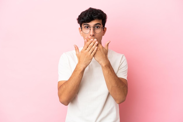 Young Argentinian man isolated on pink background covering mouth with hands