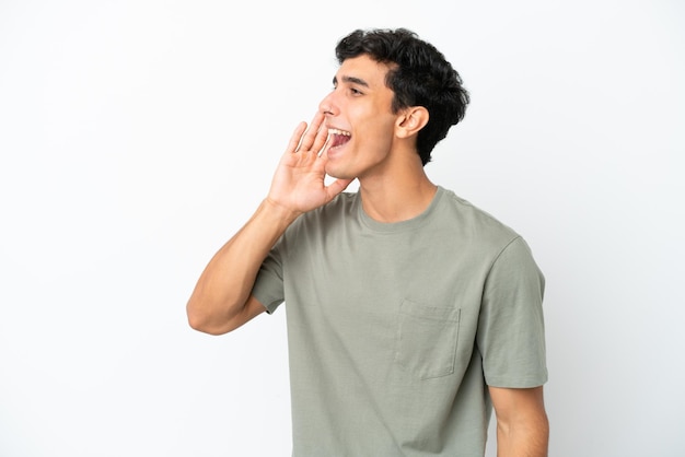 Young Argentinian man isolated on white background shouting with mouth wide open to the side