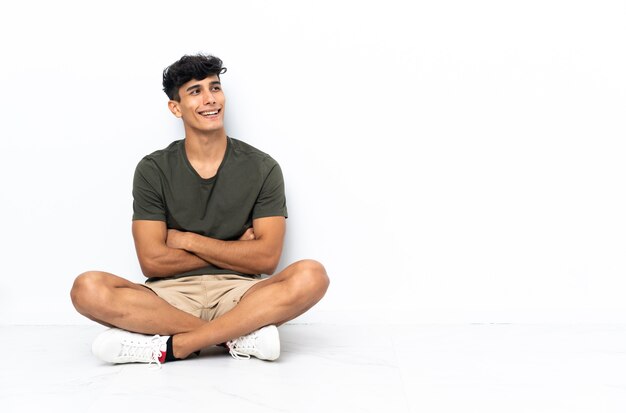 Young Argentinian man sitting on the floor happy and smiling