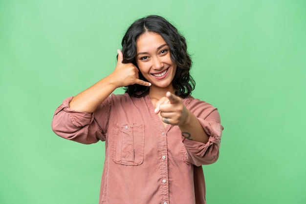 Young Argentinian woman over isolated background making phone gesture and pointing front