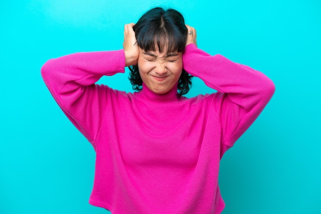 Young Argentinian woman isolated on blue background frustrated and covering ears