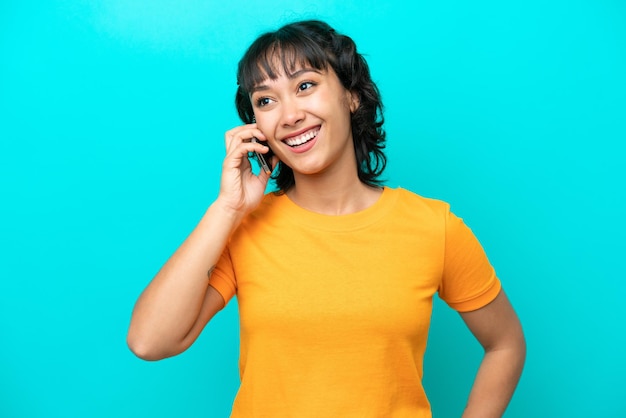 Young Argentinian woman isolated on blue background keeping a conversation with the mobile phone