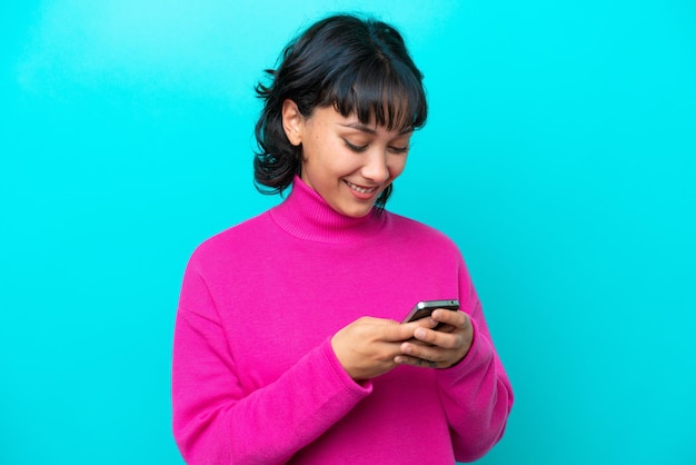 Young Argentinian woman isolated on blue background sending a message with the mobile