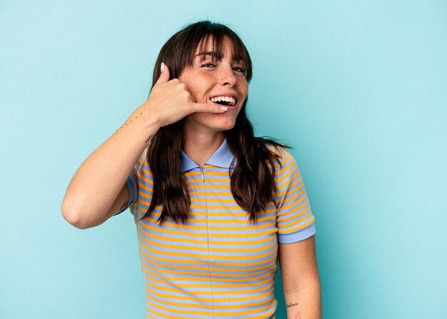 Young Argentinian woman isolated on blue background showing a mobile phone call gesture with fingers.