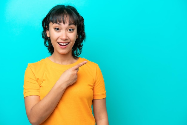 Young Argentinian woman isolated on blue background surprised and pointing side