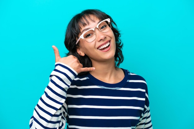 Young Argentinian woman isolated on blue background With glasses and doing phone gesture