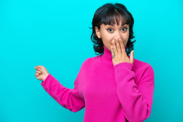 Young Argentinian woman isolated on blue background with surprise expression while pointing side