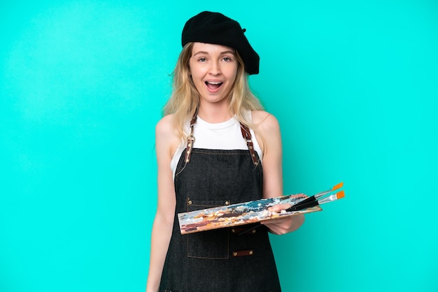 Young artist caucasian woman holding a palette isolated on blue background with surprise facial expression