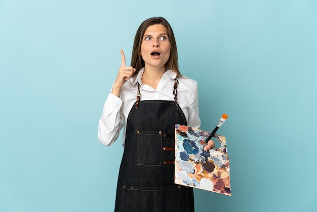 Young artist Slovak woman isolated on blue background thinking an idea pointing the finger up