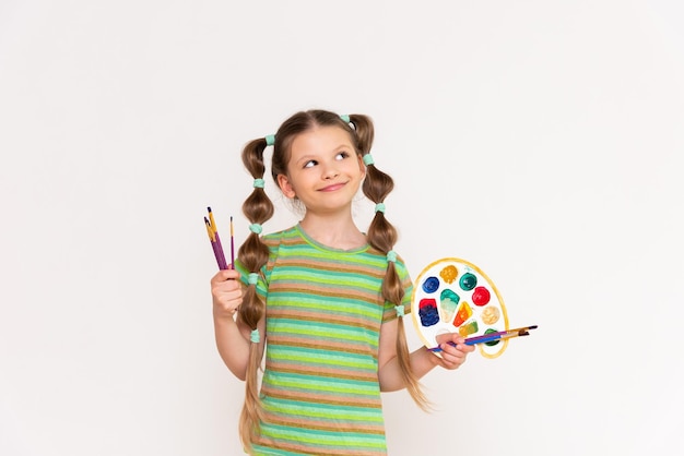 A young artist with a palette of paints for brushes for drawing on a white isolated background