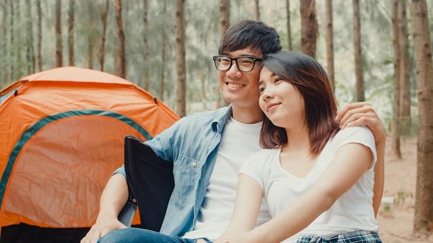 Young asia campers couple sitting in chairs by tent in forest