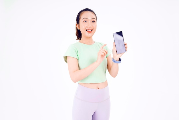 Young Asia lady show empty smart phone screen with positive expression smiles broadly dressed in casual clothing feeling happiness on blue background Mobile phone with white screen in female hand