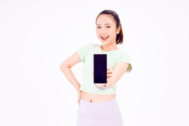 Young Asia lady show empty smart phone screen with positive expression smiles broadly dressed in casual clothing feeling happiness on blue background Mobile phone with white screen in female hand