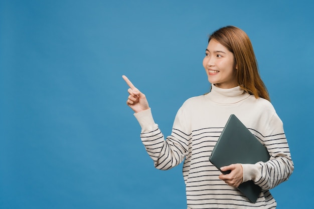 Young Asia lady using laptop with positive expression, smiles broadly, dressed in casual clothing feeling happiness and stand isolated on blue wall