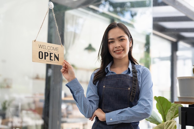 Young Asia manager girl changing a sign from closed to open sign on door cafe looking outside waiting for clients after lockdown Owner small business food and drink business reopen again concept