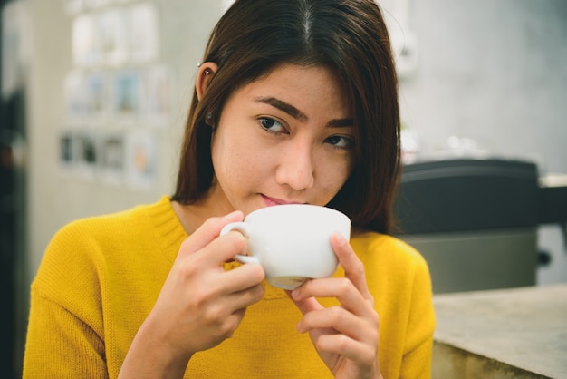 young asian adult woman drinking coffee smiling in cafe.