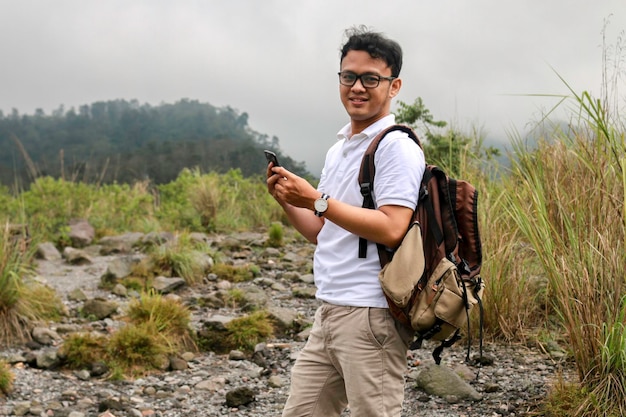 Young asian backpacker man is happy and smile when he looking smartphone when traveling in mountain