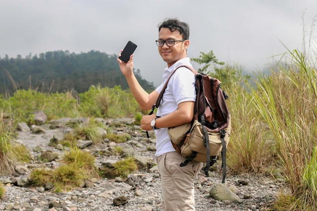 Young asian backpacker man is happy and smile when he showing smartphone when traveling in mountain