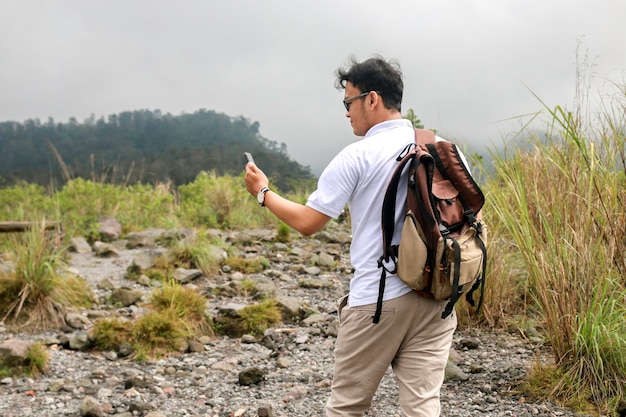 Young asian backpacker man is happy taking vlog or video with smartphone when traveling in mountain