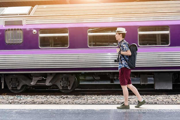 Young Asian backpacker man is walking to take a train at the station