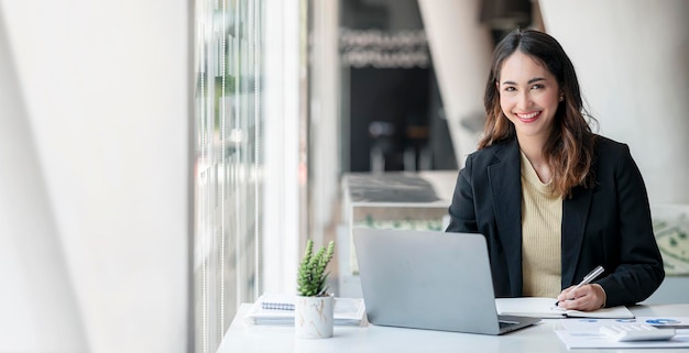 Young asian beautiful and charming busineswoman smiling and working on laptop computer at office