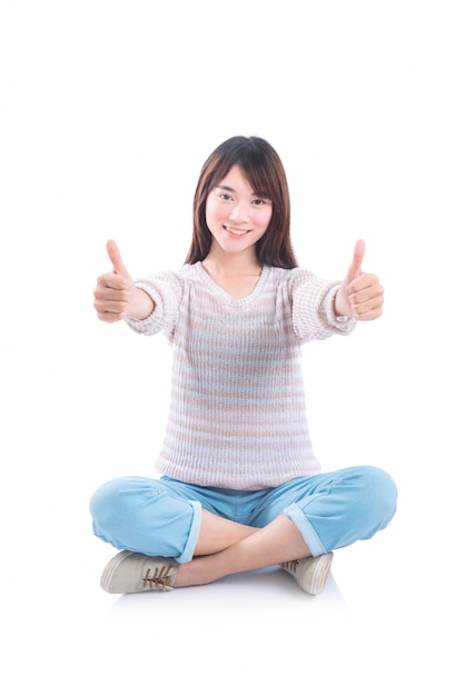 Young asian beautiful girl sitting on the floor and showing thumbs up over white background