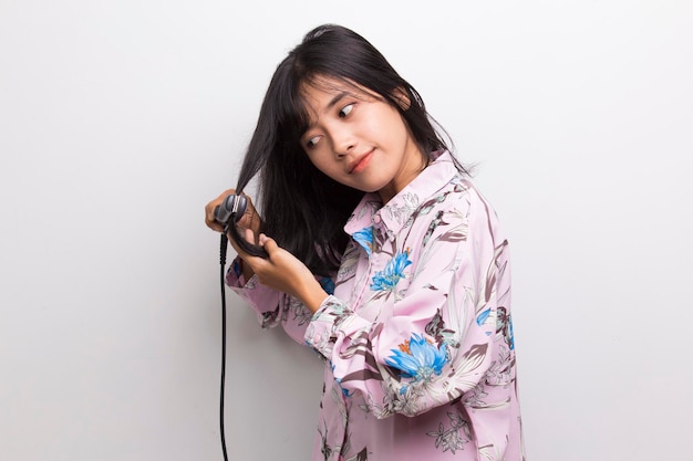 young asian beautiful happy woman straightening hair with hair straightener on white background