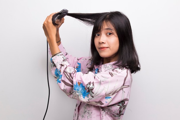 young asian beautiful happy woman straightening hair with hair straightener on white background