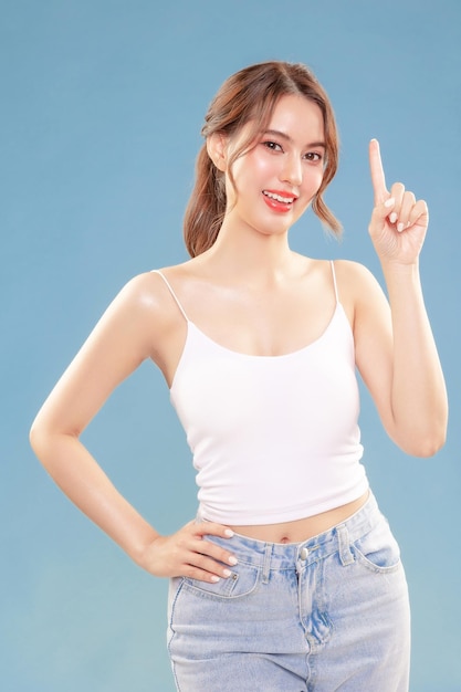 Young Asian beauty happy woman pull back hair with Koreans makeup style on face and perfect clean skin show point finger on isolated blue background