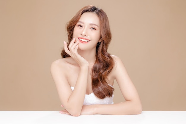 Young Asian beauty woman curly long hair with korean makeup style touch her face and perfect skin on isolated beige background Facial treatment Cosmetology plastic surgery