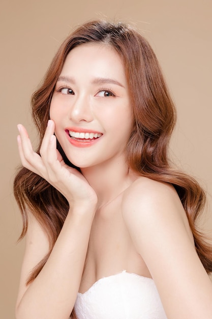 Young Asian beauty woman curly long hair with korean makeup style touch her face and perfect skin on isolated beige background Facial treatment Cosmetology plastic surgery