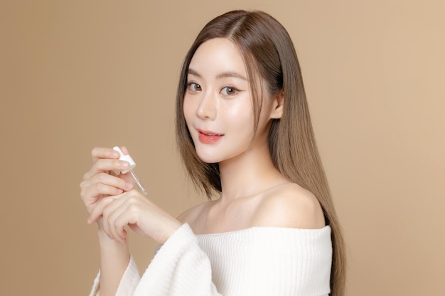 Young Asian beauty woman long hair with korean makeup style on face and perfect clean skin on isolated beige background Female model apply serum Facial treatment Cosmetology plastic surgery