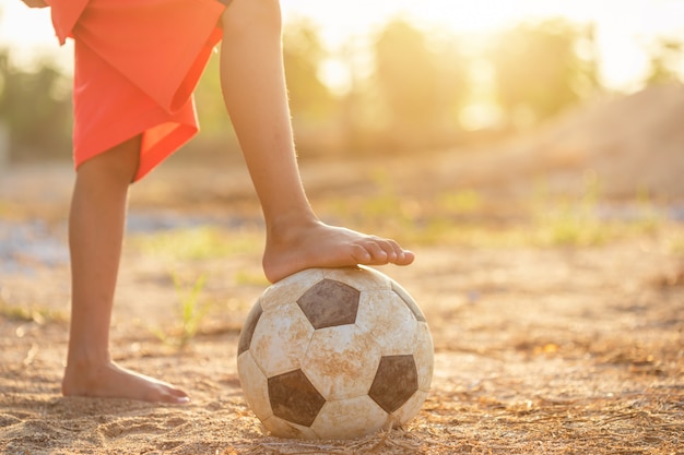 Photo young asian boy playing with old and dirty classic soccer ball in the morning