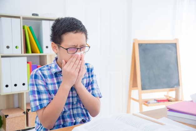 Young asian boy wipe his nose by tissue paper in his classroom at school